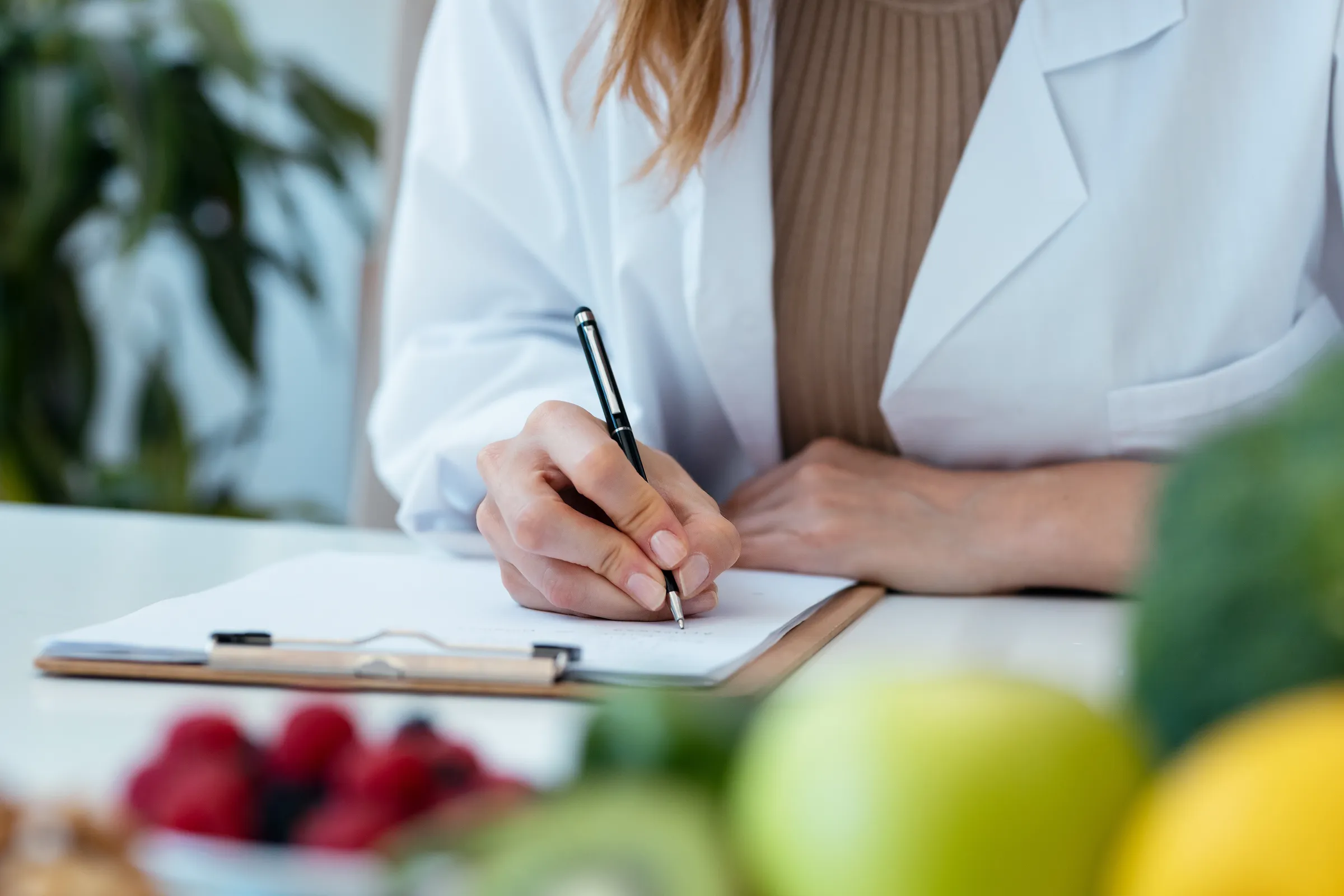 A clinician taking notes beside fresh fruit and vegetables