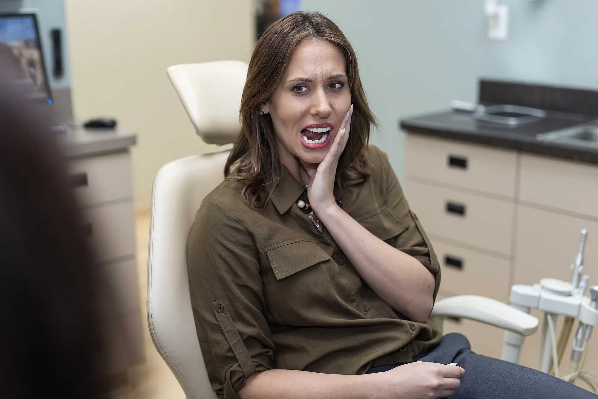 Woman experiencing tooth pain while sitting in a dental chair